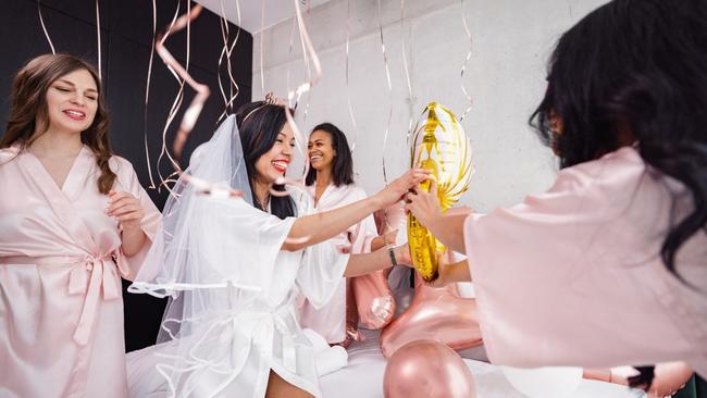 A Latin bride-to-be and her diverse friends having fun and smiling while playing with the balloon decorations in the bedroom. They are jumping on the bed and having fun. Fun bachelorette activities.