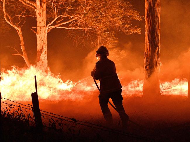 TOPSHOT - This picture taken on December 31, 2019 shows a firefighter hosing down trees and flying embers in an effort to secure nearby houses from bushfires near the town of Nowra in the Australian state of New South Wales. - Fire-ravaged Australia has launched a major operation to reach thousands of people stranded in seaside towns after deadly bushfires ripped through popular tourist areas on New Year's Eve. (Photo by SAEED KHAN / AFP)