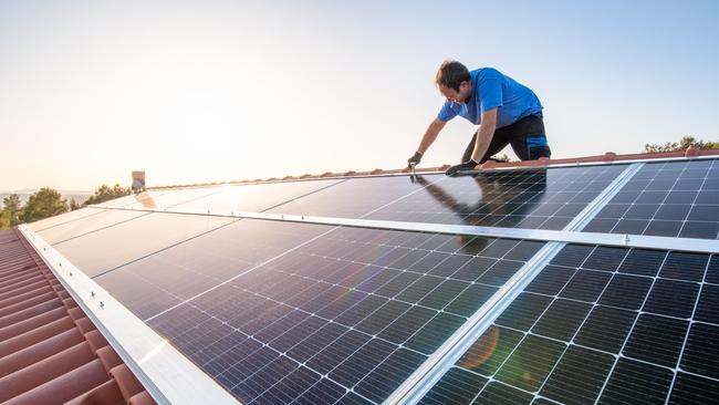 kneeling professional fixing solar panels from the top of a house roof, side view of the roof with sun reflection