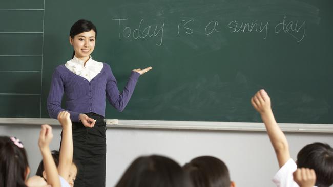 Teacher Standing By Blackboard In Chinese School Classroom