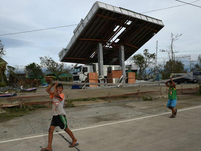 Young residents carrying a plank of wood walk past a petrol station damaged by super typhoon Haima. Picture: AFP