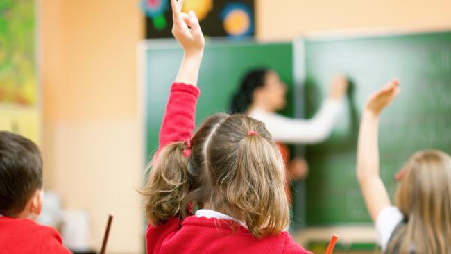 Elementary school kids raising their hands in class to answer a teacher's question.