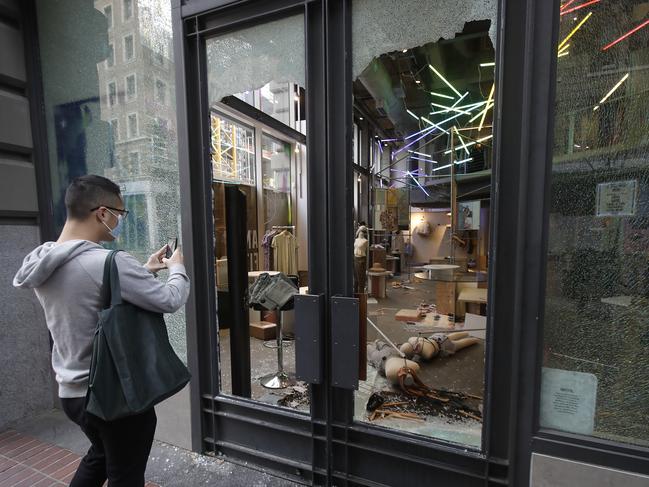 A man photographs damage at an Urban Outfitters store in San Francisco.