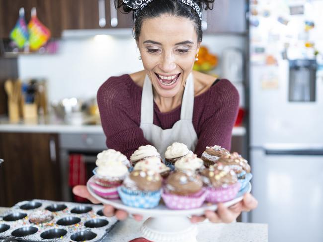 Middle aged woman holding a tray of fragrant muffins.