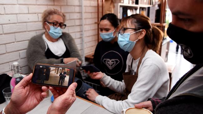 Staff and customers watch a press conference by acting Victorian Premier James Merlino on a phone at a cafe in Melbourne on Thursday.