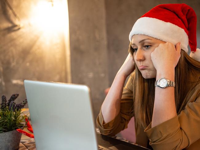 Young tired woman working on laptop wearing santa hat; Christmas spending debt generic