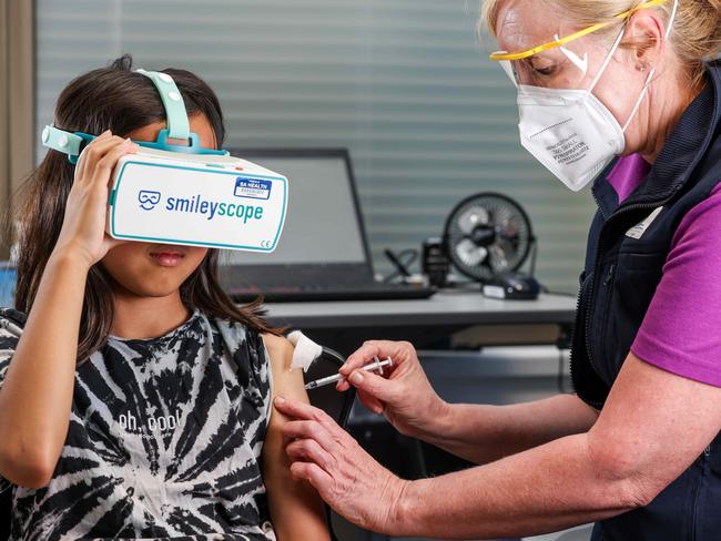 Nyomi Meth, 9, wears a Smileyscope headset while being vaccinated by nurse Maryanne Attard, Unit Manager at the Adelaide Women and Children Hospital Vaccination Clinic. Picture: Russell Millard