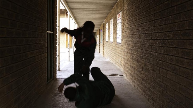 Two school kids fight in a dark passageway of their school, almost silhouette.