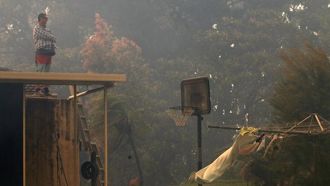 A man stands on the roof of his house as a bushfire approaches on Lemon Tree Passage Rd, Salt Ash. Picture: AAP