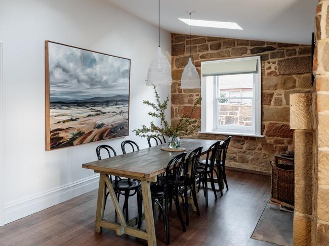 Raffah House’s dining room, featuring the original, thick, exposed sandstone walls and a painting by Hobart-artist Chris Bury titled the Southern Midlands.