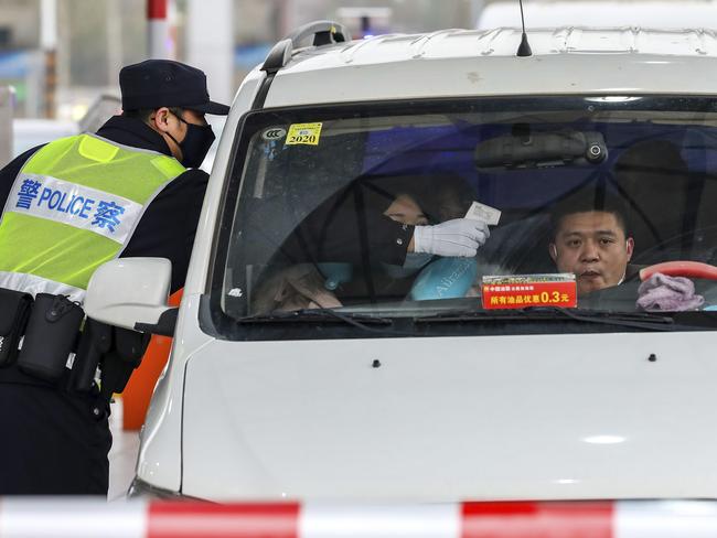 A policeman using a digital thermometer to take a driver’s temperature at a highway toll gate check out in Wuhan. Picture: Chinatopix via AP