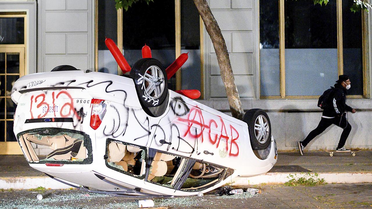 A car lays flipped, smashed and tagged with graffiti in Oakland, California. Picture: Noah Berger/AP