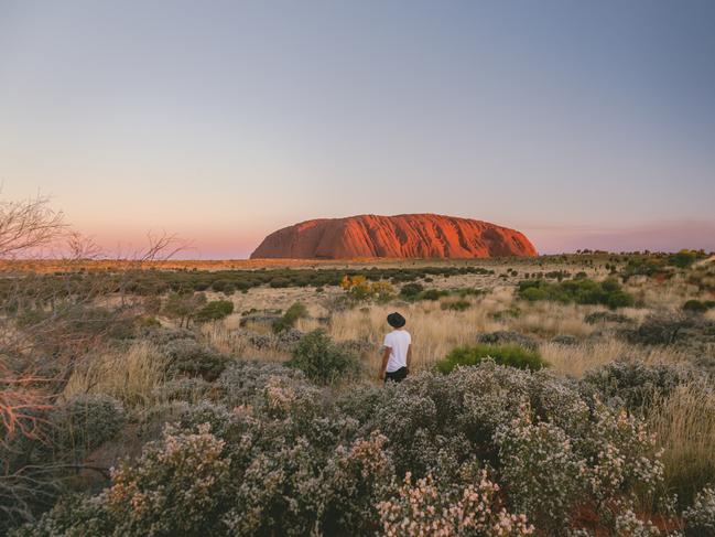 ESCAPE: A visitor stands in the desert landscape looking at Uluru during sunset.One of the great natural wonders of the world, Uluru towers above the surrounding landscape. Uluru is not only a spectacular natural formation, but its a deeply spiritual place. You can feel a powerful presence the moment you first set eyes on it. Picture: Tourism NT/Jason Van Miert