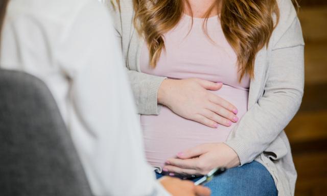 Caucasian pregnant woman is discussing something during a childbirth class or pregnancy support group. Focus on belly, no faces.