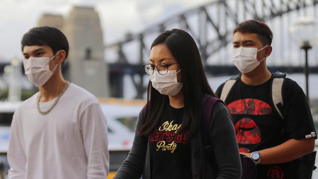 People wear face masks in front of the Sydney Harbour Bridge in Sydney, Monday, March 9, 2020. AAP, Steven Saphore