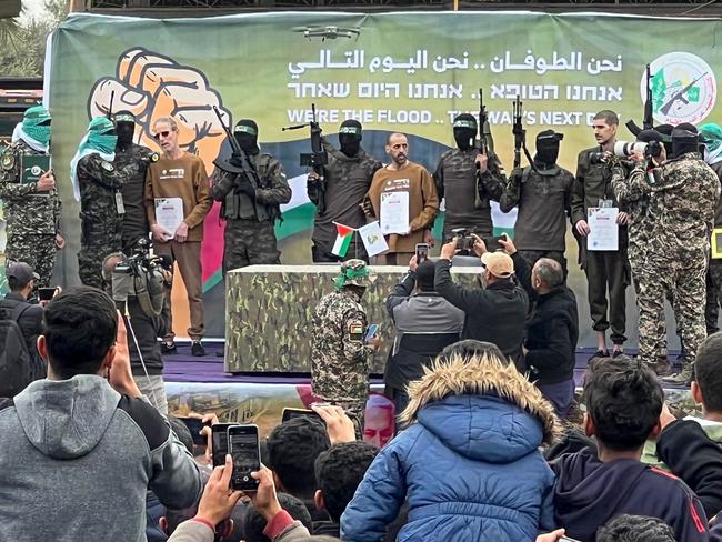 Palestinian Hamas fighters escort Israeli hostages (L-R) Ohad Ben Ami, Or Levy and Eli Sharabi on a stage before handing them over to a Red Cross team in Deir el-Balah, central Gaza, on February 8, 2025, as part of the fifth hostage-prisoner exchange of a fragile ceasefire. The swap comes after US President Donald Trump proposed clearing out the Gaza Strip of its inhabitants and for the United States to take over the Palestinian territory -- a plan that has sparked global uproar and been rejected by Hamas. (Photo by Bashar TALEB / AFP)