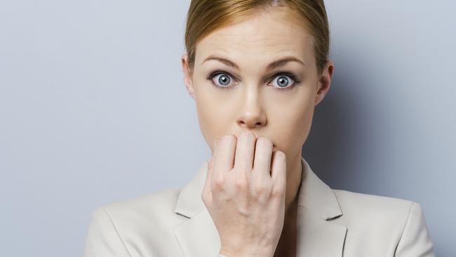 A little bit nervous. Nervous young businesswoman biting her nails while standing against grey background