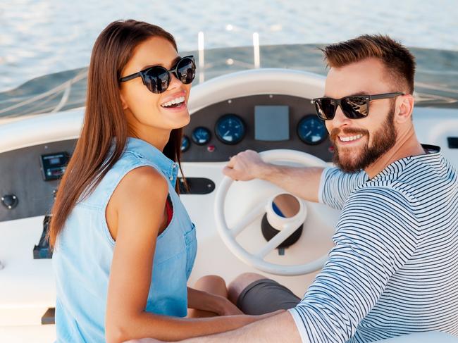 Cheerful young couple looking at camera and smiling while driving yacht. Boating generic.