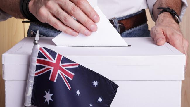 A man inserting a ballot to a ballot box. Australian flag in front of it.