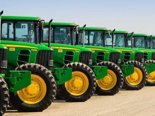 A row of John Deere farm tractors park in a row at a Ritchie Bros Auction in Tulare, California.