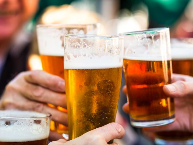 Close up color image depicting a group of people celebrating with a toast. The people cheers their glasses of beer (pints of beer) together in a gesture of celebration, togetherness and happiness. The people are defocused in the background, while focus is on the glasses of beer in the foreground. Room for copy space.