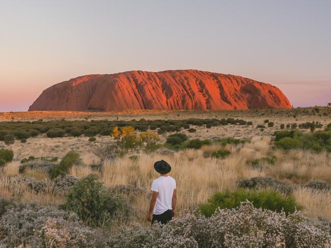 ESCAPE: A visitor stands in the desert landscape looking at Uluru during sunset.One of the great natural wonders of the world, Uluru towers above the surrounding landscape. Uluru is not only a spectacular natural formation, but its a deeply spiritual place. You can feel a powerful presence the moment you first set eyes on it. Picture: Tourism NT/Jason Van Miert
