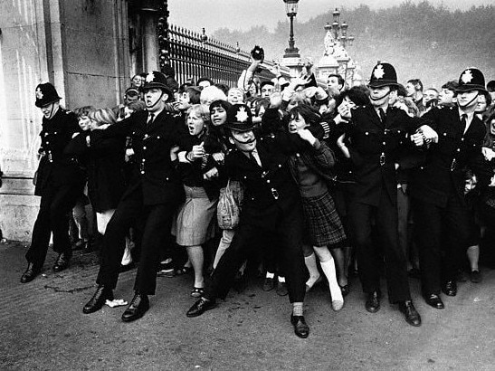 26 Oct 1965, London, England, UK --- A crowd of excited fans rush against a line of police officers at the gates of Buckingham Palace, in hopes of a glimpse of the 1960s rock supergroup, The Beatles. The band arrives for acceptance into the Order of the British Empire by Queen Elizabeth II. --- Image by � Hulton-Deutsch Collection/CORBIS