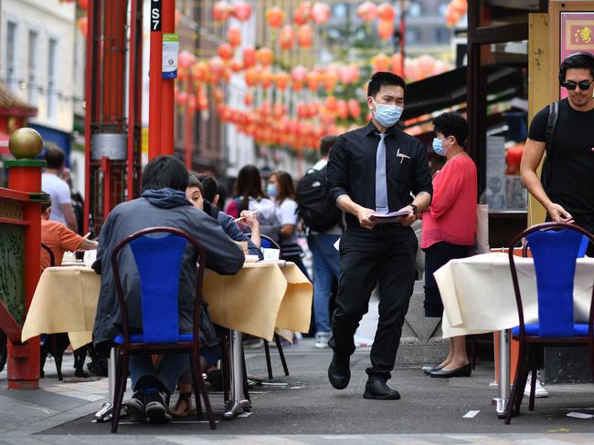 A waiter wearing a protective face mask serves customers eating lunch at the outside tables of a restaurant in the chinatown area of Soho in London. Picture: AFP