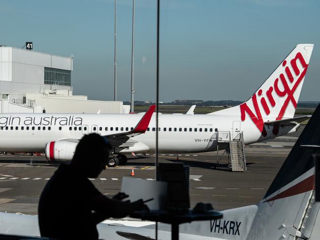 A man sits at a cafe in front of a Virgin Australia aircraft at Sydney Airport, Sydney, Friday, June 19, 2020. (AAP Image/James Gourley) NO ARCHIVING