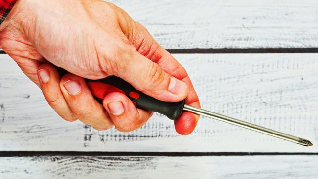 Screwdriver, generic, man. Handyman wearing a classic work shirt is holding a screwdriver in his hand. part of the body only, unrecognizable person with rough skin. Close-up capture.