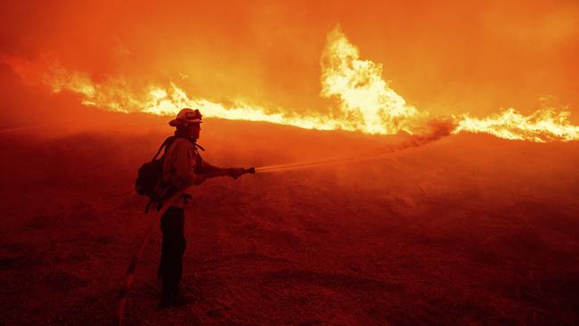 A firefighter sprays water as he monitors flames caused by the Hughes Fire along a roadside in Castaic. Picture: AP