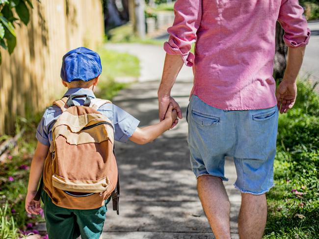 Rear view of an Australian aboriginal father taking his son to school, they are walking in the street holding hands.