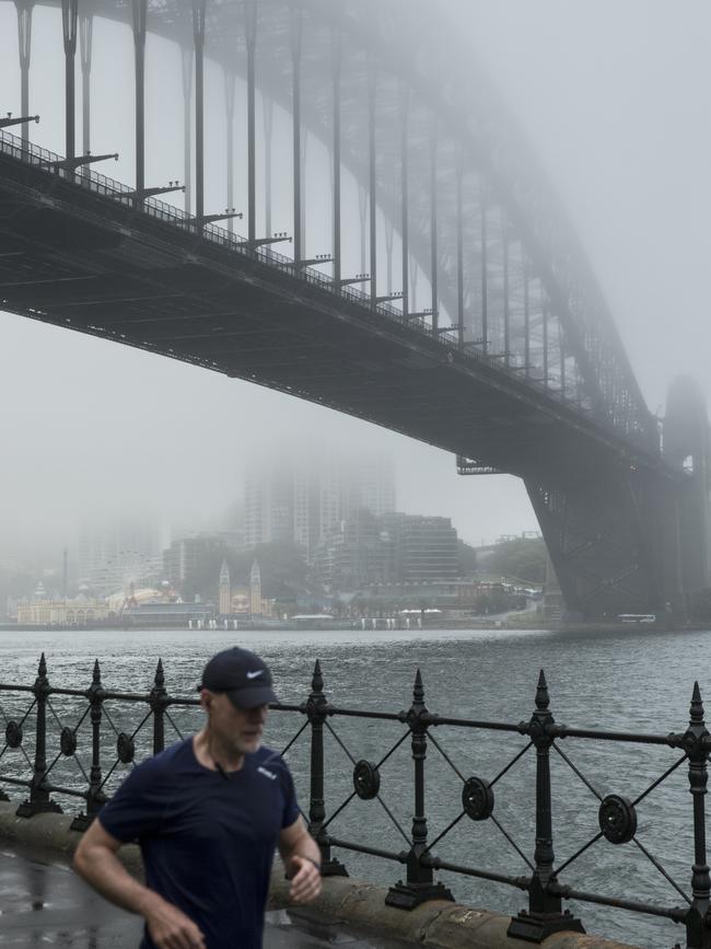 A runner pictured at Dawes Point with the Sydney Harbour Bridge cloaked in fog this morning. Picture: NCA NewsWire / Damian Shaw