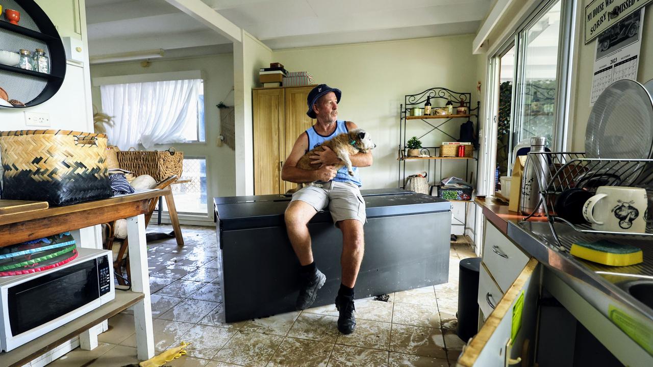 Chris Tress sits on his upturned refrigerator with his dog Peggy in his kitchen that was flooded in Mimosa Street, Holloways Beach. Picture: Brendan Radke