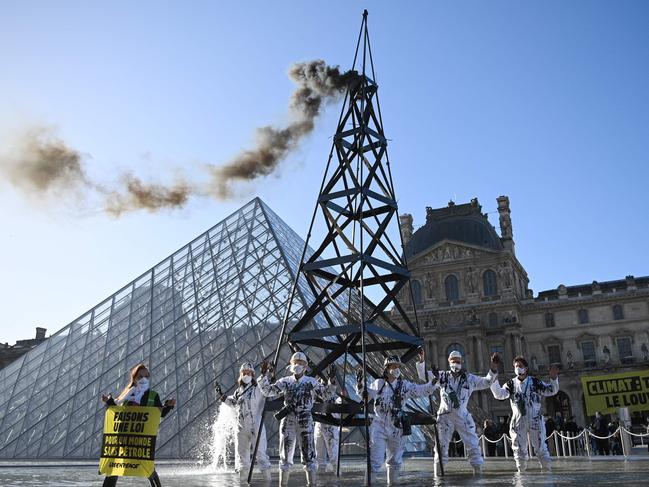 Greenpeace activists wearing the uniform of petroleum workers stand beside a smoking 'oil well tower' during an action in front of The Louvre Museum Pyramid in Paris. Picture: Anne-Christine Poujoulat/AFP