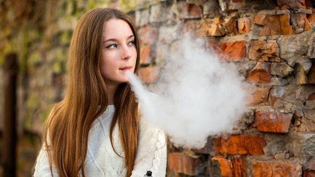 Vaping teenager. Young pretty white caucasian teenage girl with problem skin smoking an electronic cigarette the ruined brick wall on the street in the autumn. Bad habit. Vape activity.