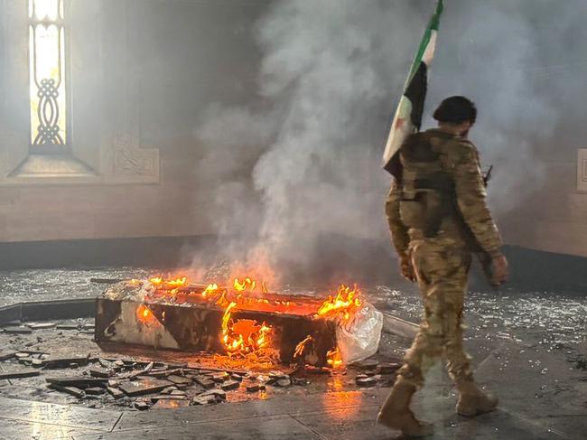 TOPSHOT - Rebel fighters stand next to the burning gravesite of Syria's late president Hafez al-Assad at his mausoleum in the family's ancestral village of Qardaha in the western Latakia province on December 11, 2024, after it was stormed by opposition factions. The father and predecessor of Syria's ousted president Bashar al-Assad died in 2000. (Photo by Aaref WATAD / AFP)