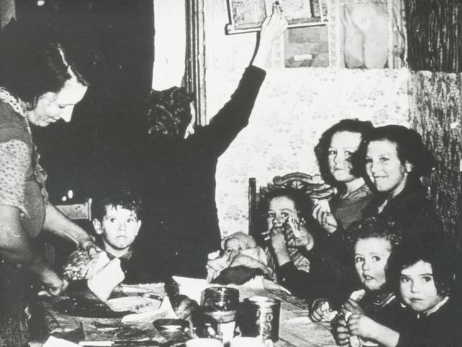 A woman and her eight children cram into the kitchen in their home in an inner suburban slum. F. Oswald Barnett collection, State Library of Victoria