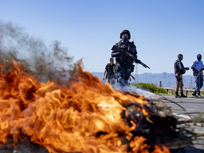 Police gather behind a burning barricade near Cape Town, South Africa, Wednesday, April 22, 2020 as Heinz Park residents demanded food parcels from the government. Residents claim that due to the current coronavirus lockdown in South Africa they are unable to go out and look for work and food. (AP Photo)