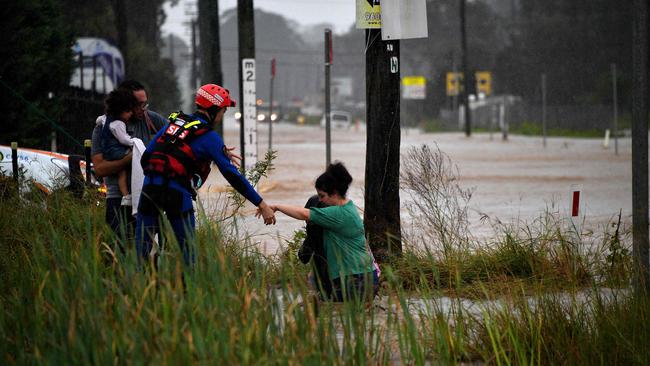 A rescue worker helps residents cross a flooded road during heavy rain in western Sydney. Picture: AFP