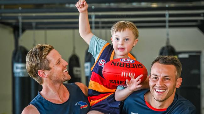 13/2/23 - Rory Sloane and Tom Doedee from the Crows with Koa Fahey, 6, a young boy with Down Syndrome. Pictured at Crows headquarters in West Lakes. Picture: Naomi Jellicoe