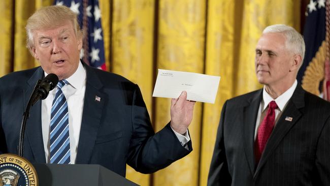 Donald Trump, flanked by Vice-President Mike Pence, yesterday waves the welcome letter by Barack Obama.