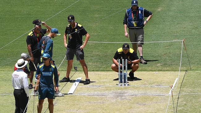 Australian coach Justin Langer speaks with an umpire as Nathan Lyon inspects the pitch prior to play on day three. Picture: AAP