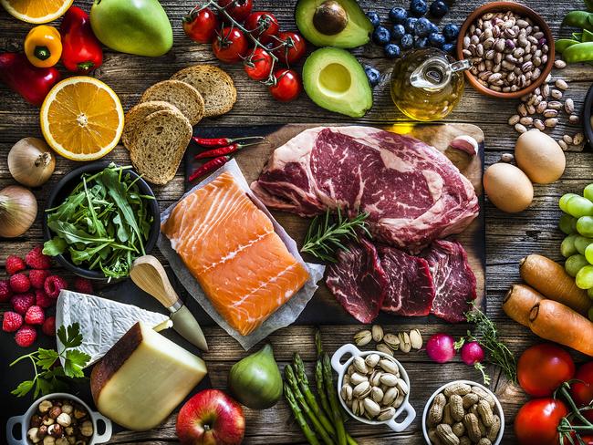 Food backgrounds: top view of a rustic wooden table filled with different types of food. At the center of the frame is a cutting board with beef steak and a salmon fillet and all around it is a large variety of food like fruits, vegetables, cheese, bread, eggs, legumes, olive oil and nuts. DSRL studio photo taken with Canon EOS 5D Mk II and Canon EF 70-200mm f/2.8L IS II USM Telephoto Zoom Lens