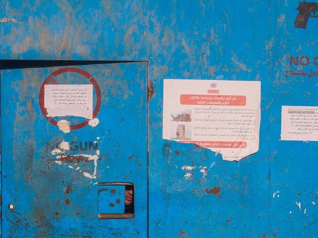 TOPSHOT - A man peeks out of an opening in the gate of an aid distribution center of the United Nations Relief and Works Agency (UNRWA) in the Nuseirat camp for Palestinian refugees in the central Gaza Strip on October 29, 2024, amid the ongoing war between Israel and Hamas. Israel faced a mounting international backlash on October 29, after its parliament approved a bill banning the main UN aid agency for the devastated Gaza Strip. (Photo by Eyad BABA / AFP)