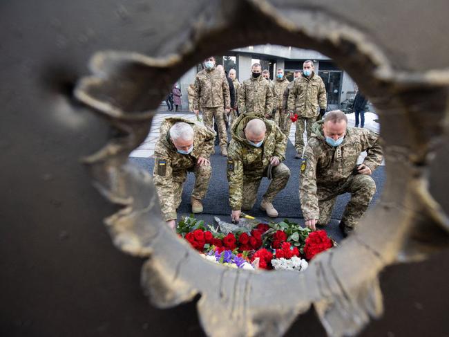 TOPSHOT - This handout picture taken and released by Ukrainian President press-service on January 20, 2022 shows Ukrainian military forces servicemen laying flowers to Memorial Bell, located on the territory of the Ministry of Defense in Kyiv, as they take part in honoring the memory of Ukrainian servicemen who died on this day for freedom, independence and territorial integrity of the state. - The names of 54 servicemen, who died in different years of the war on east of the country, among them - 51 soldiers who died on January 20, 2015, defending the Donetsk airport, were announced during the ceremony. (Photo by Ukrainian President press-service / AFP) / RESTRICTED TO EDITORIAL USE - MANDATORY CREDIT "AFP PHOTO /Ukrainian President press-service" - NO MARKETING - NO ADVERTISING CAMPAIGNS - DISTRIBUTED AS A SERVICE TO CLIENTS