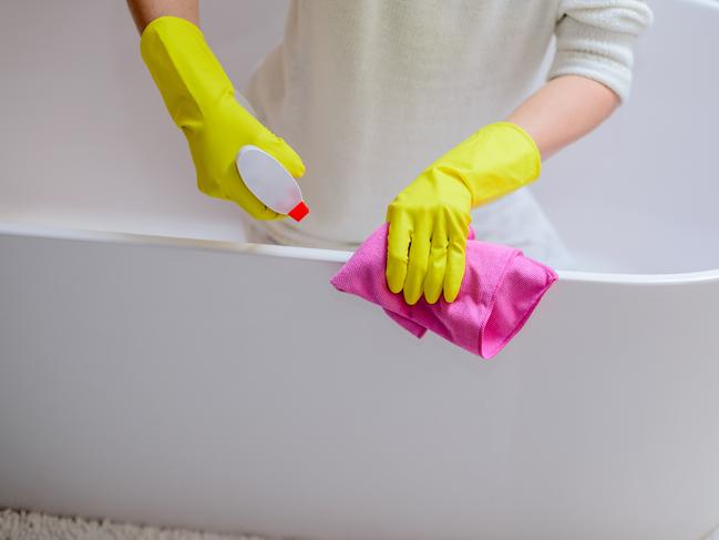 Female hands with yellow rubber protective gloves cleaning bath with pink cloth and spray detergent. Spring cleaning