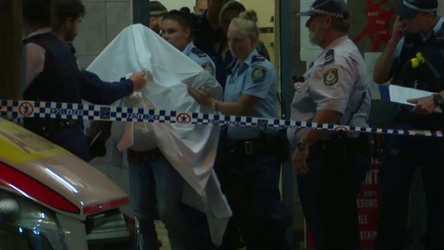 A police officer cradles the girl’s head as she is carried out of the dance studio under a sheet to protect her identity. Picture: TVN