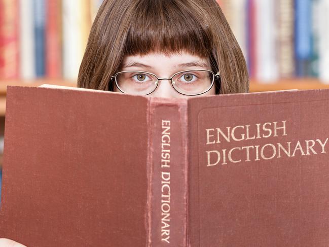 girl with spectacles looks over English Dictionary book and bookcase on background