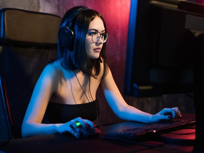 Beautiful young girl wearing glasses and gaming headset plays online game on gaming PC in dark area. Streaming online games on internet. ISTOCK IMAGE